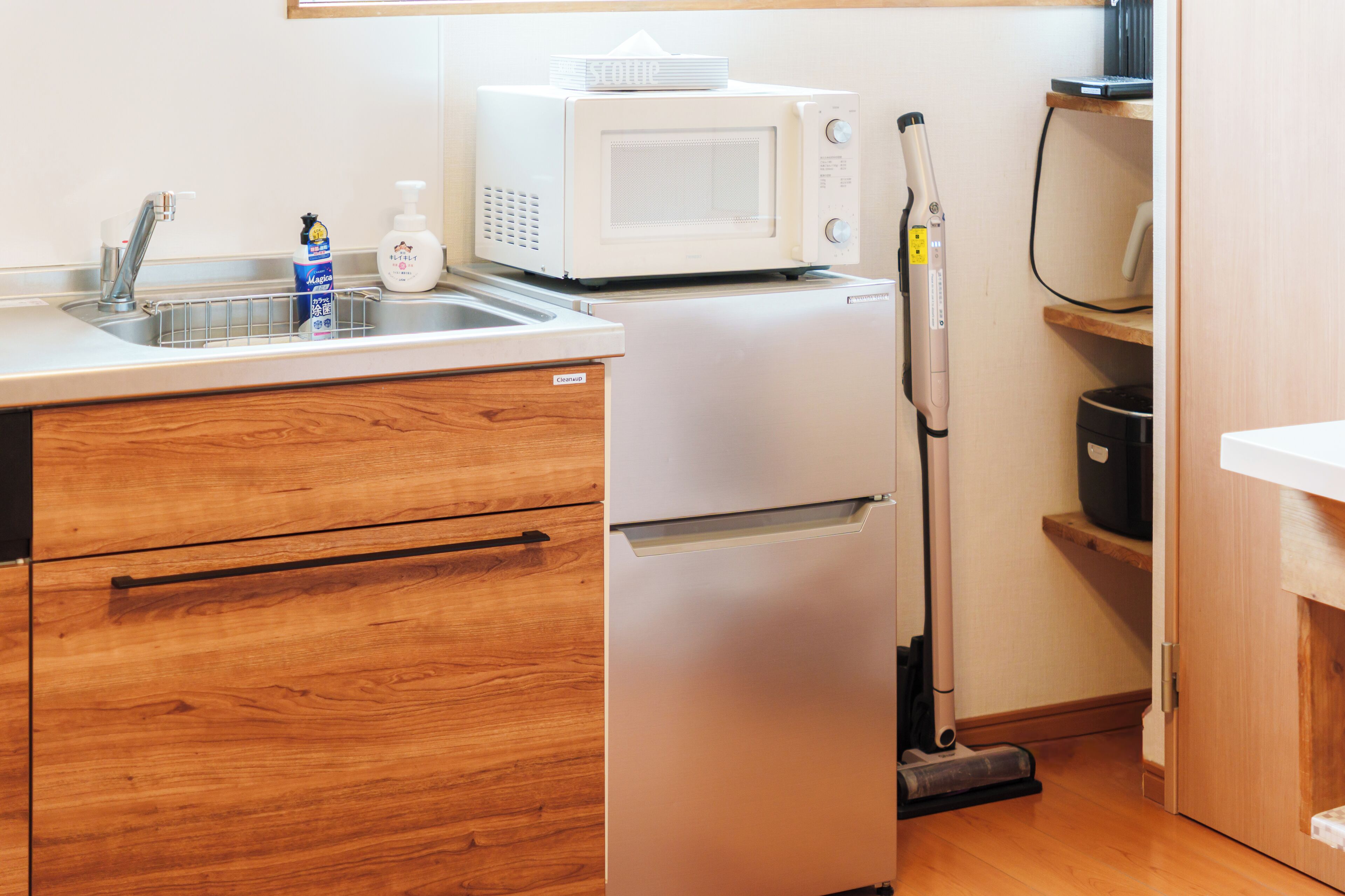 A compact kitchen with a microwave, sink, and a vacuum cleaner.