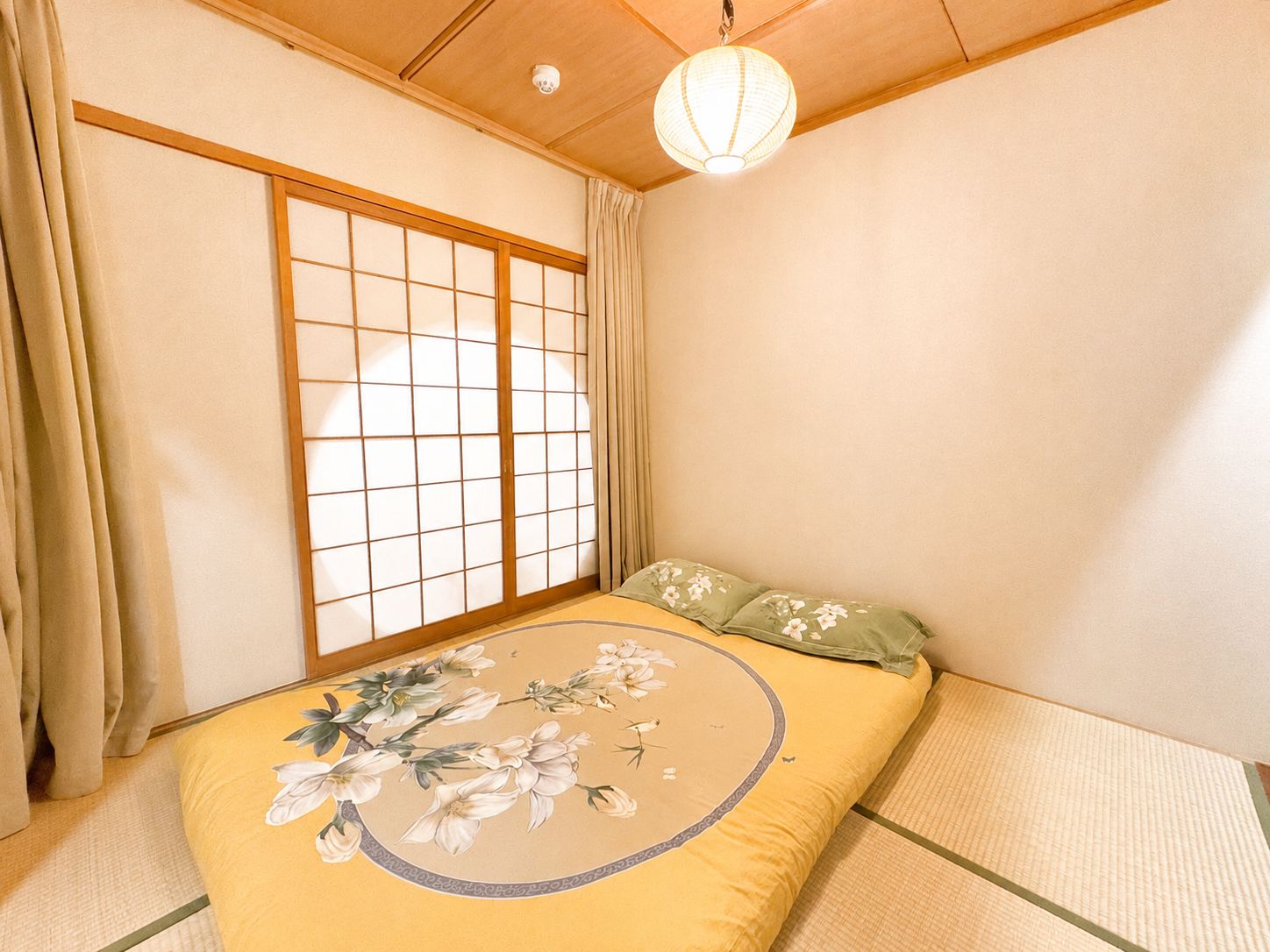 A traditional Japanese room with tatami flooring, a shoji screen, a bed with floral bedding, and a hanging paper lantern.