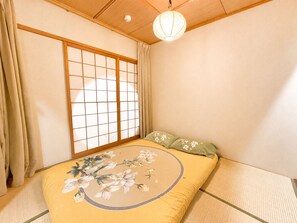 Una habitación japonesa tradicional con suelo de tatami, un biombo shoji, una cama con ropa de cama floral y un farolillo de papel colgante.