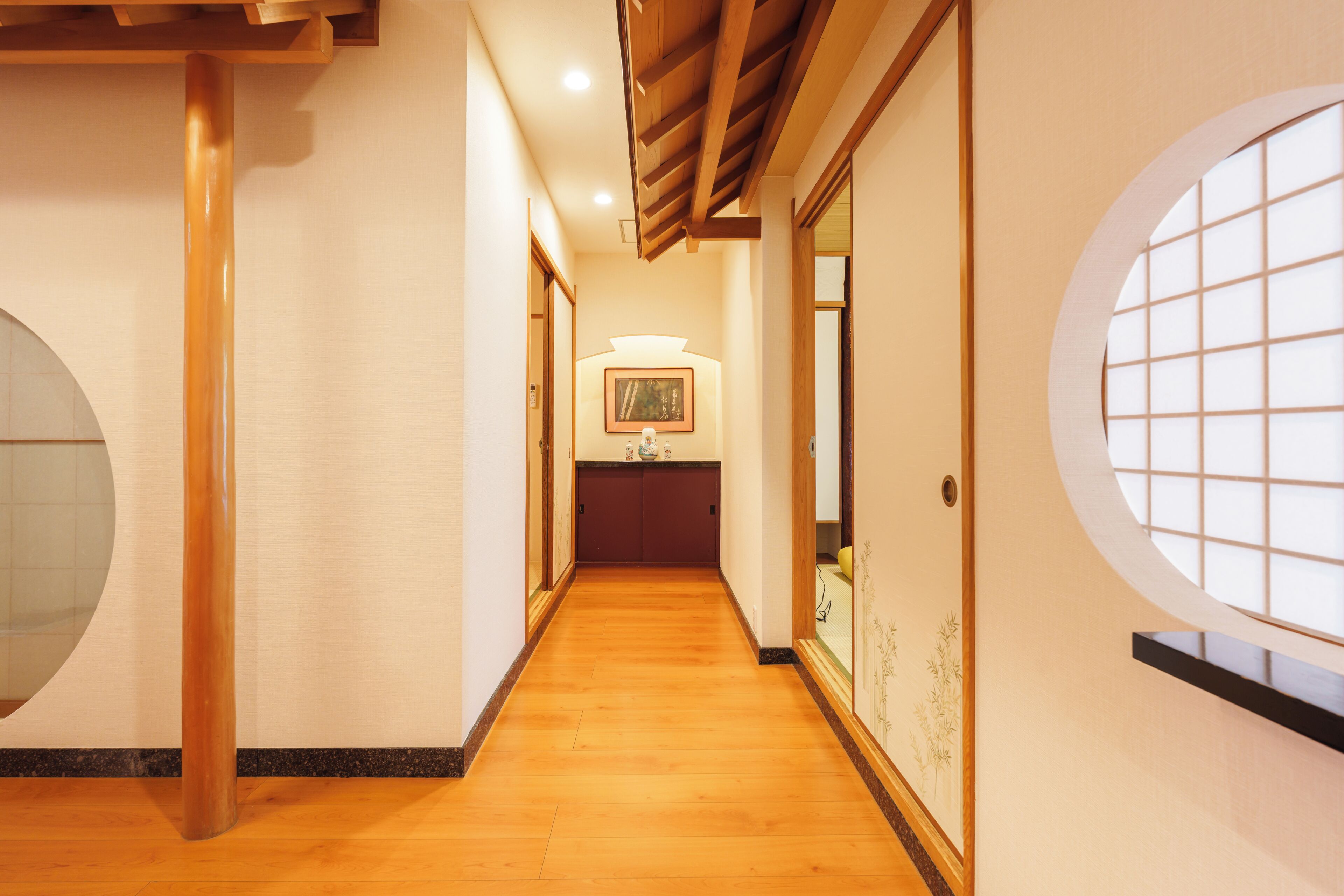 A hallway with wooden flooring, a wooden ceiling, and a large circular window on the right.