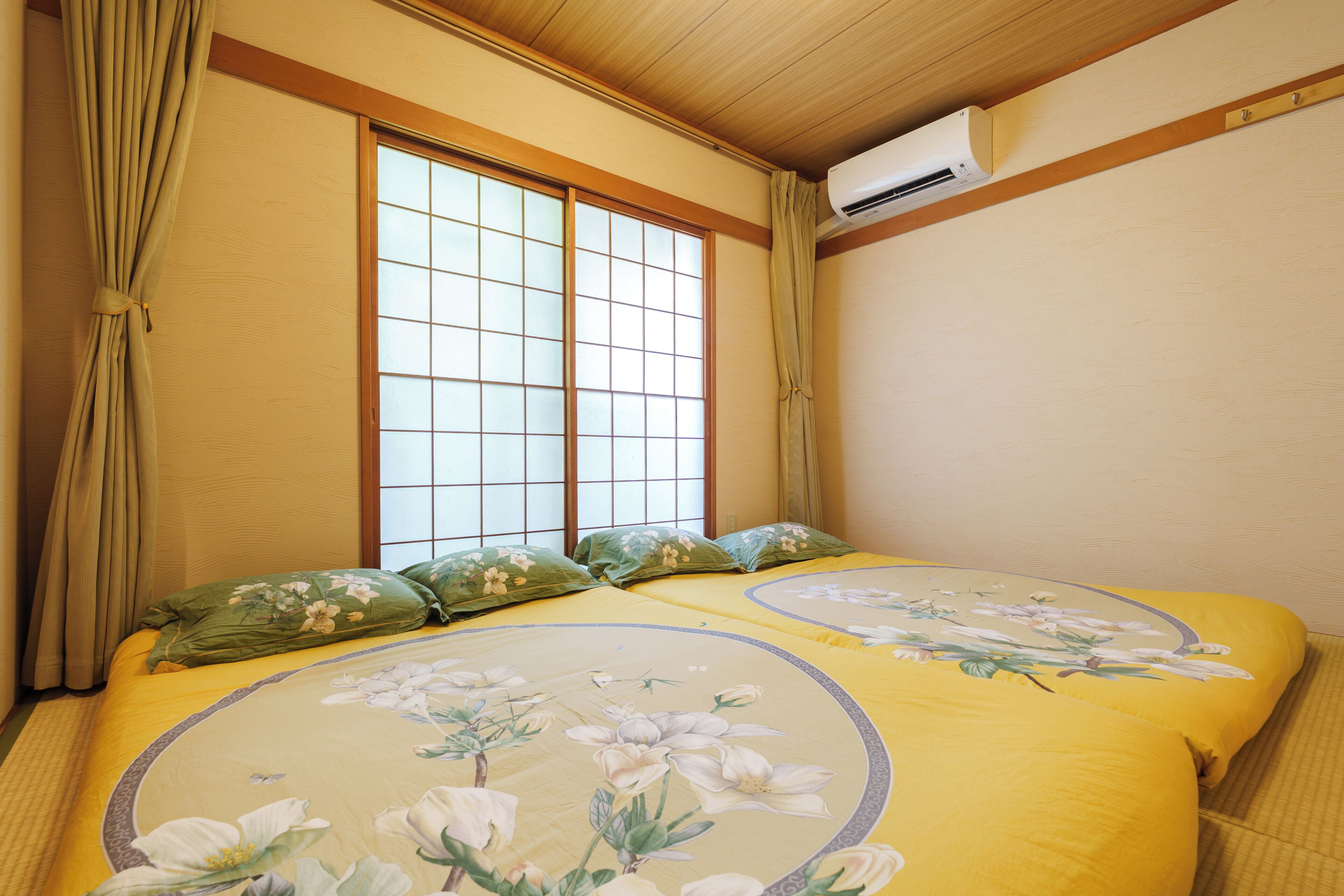A room with two beds, a large window, and an air conditioning unit.
