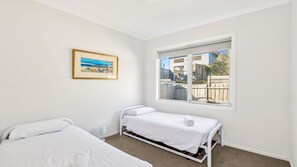 Ein Schlafzimmer mit einem Einzelbett, einem kleinen Nachttisch, einem Fenster mit Ausblick und einem gerahmten Bild an der Wand.