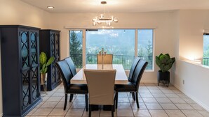 A dining area with a table and chairs, a chandelier, and a view of a mountain through large windows.