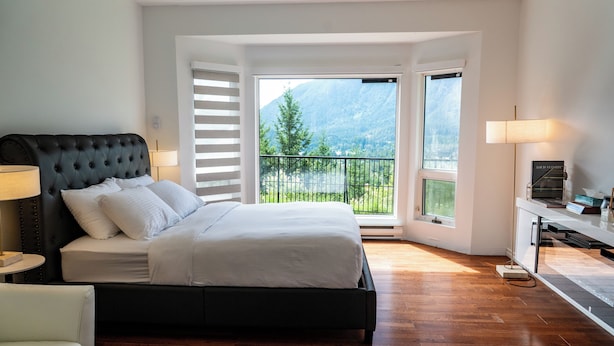A bedroom with a bed, a desk, and a view of a balcony with a mountain backdrop.