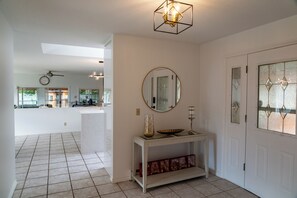 A spacious hallway with a tiled floor, a white console table with decorative items, a round mirror, and a door with frosted glass panels. - Mountain Retreat Hope - Where Mountain Meets the Sky. (Hope)