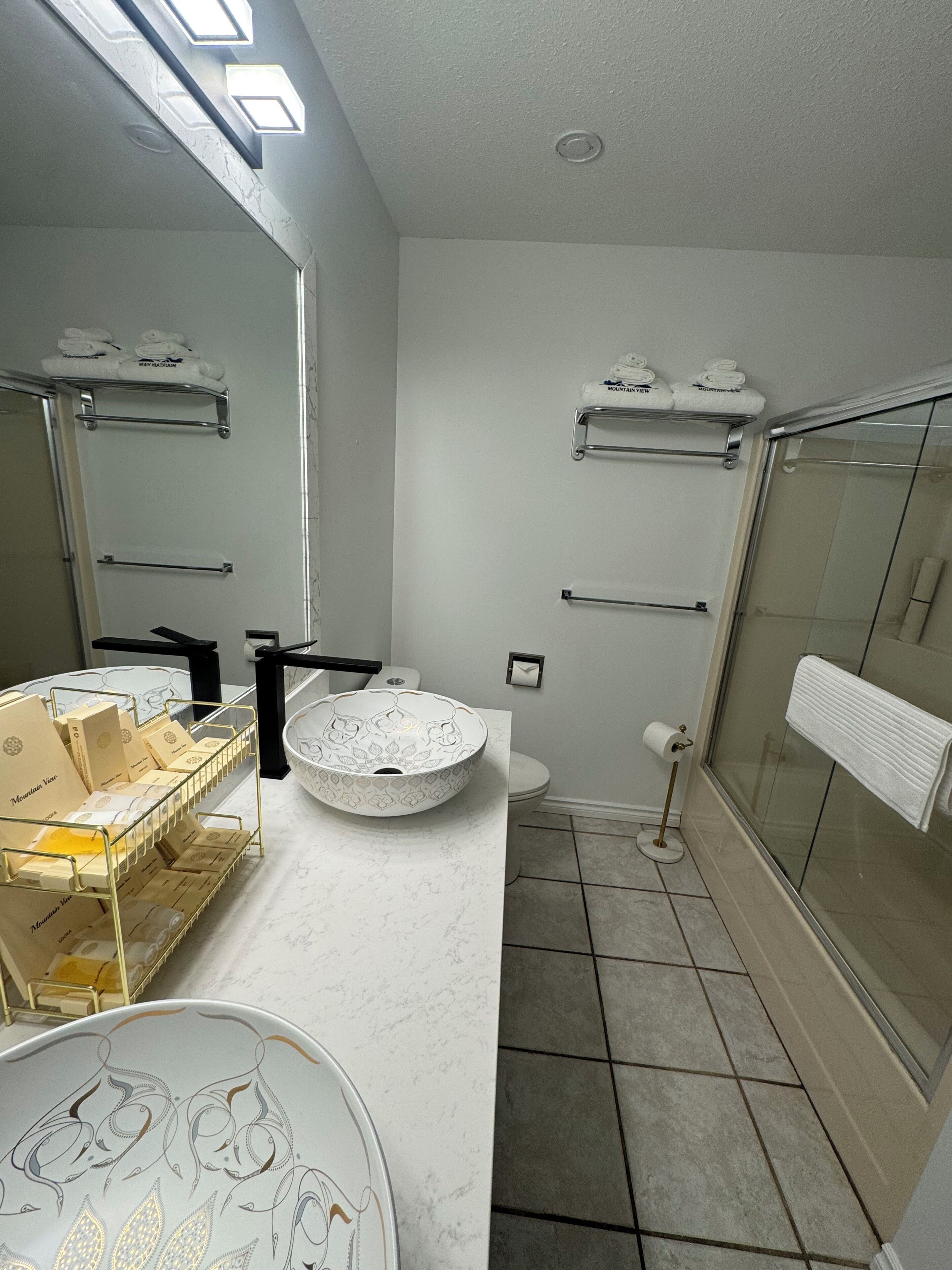 Un baño con encimera de mármol, lavamanos, inodoro, toallero y zona de ducha.