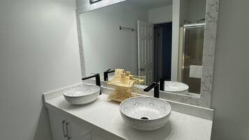 Ein Badezimmer mit einem weißen Waschtisch, zwei Aufsatzwaschbecken, einem großen Spiegel und einer beleuchteten Ablagefläche.