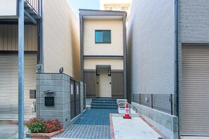 Une ruelle étroite, fermée par un portail, avec une petite marche menant à un immeuble et une clôture métallique d’un côté.
