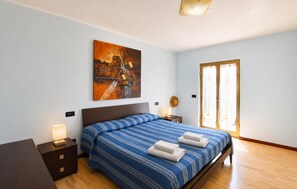 A hotel room with a bed, a nightstand, a lamp, a painting on the wall, and a door with curtains. - Gorgeous apartment in Saline Joniche with WiFi (Saline Joniche)