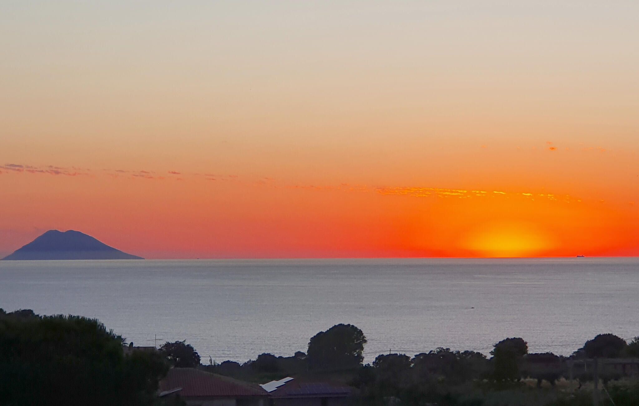 A sunset over a body of water with a mountain in the distance.