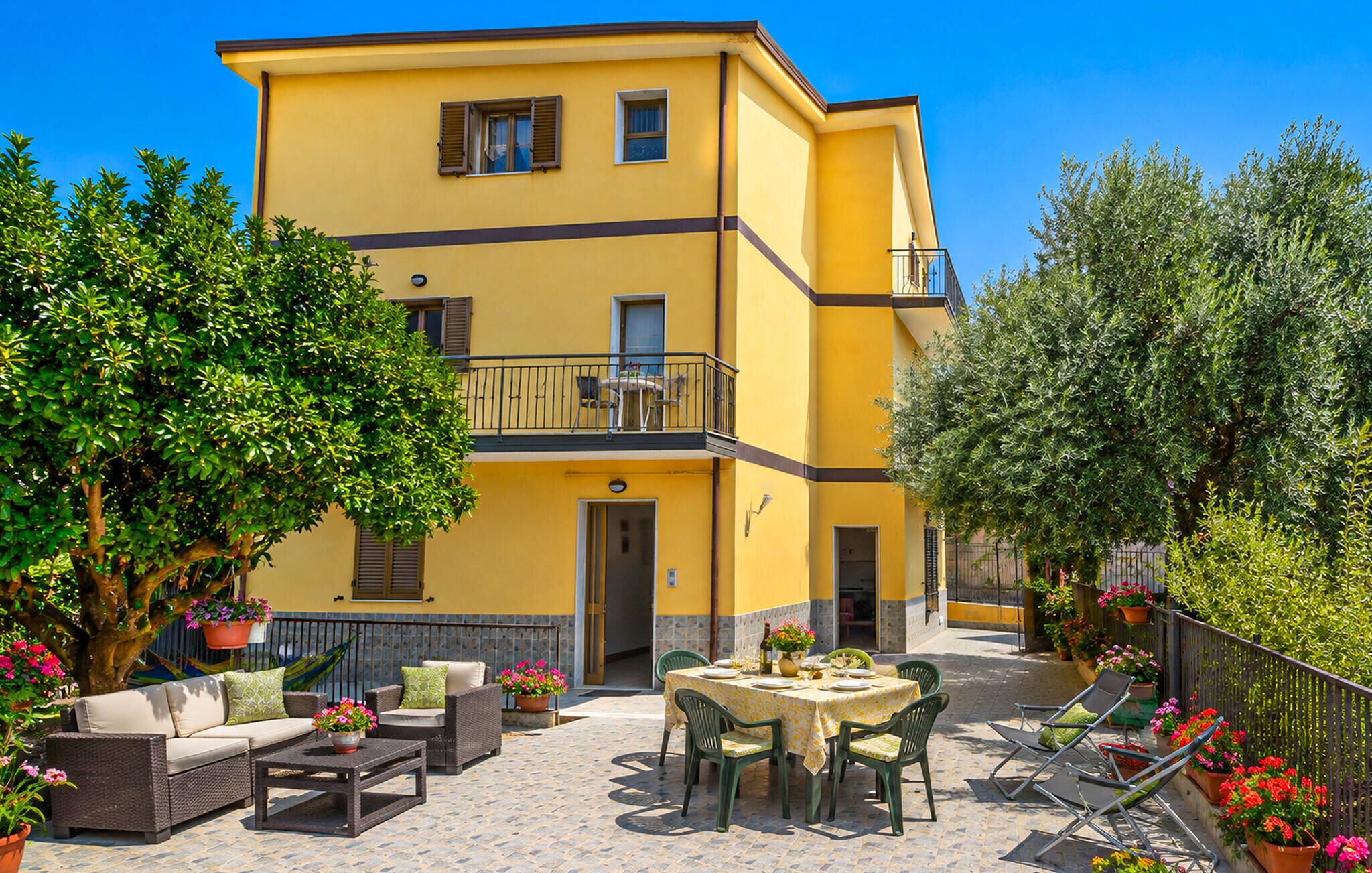 Ein gelbes Gebäude mit Balkon, Außenbereich und Blumentöpfen.