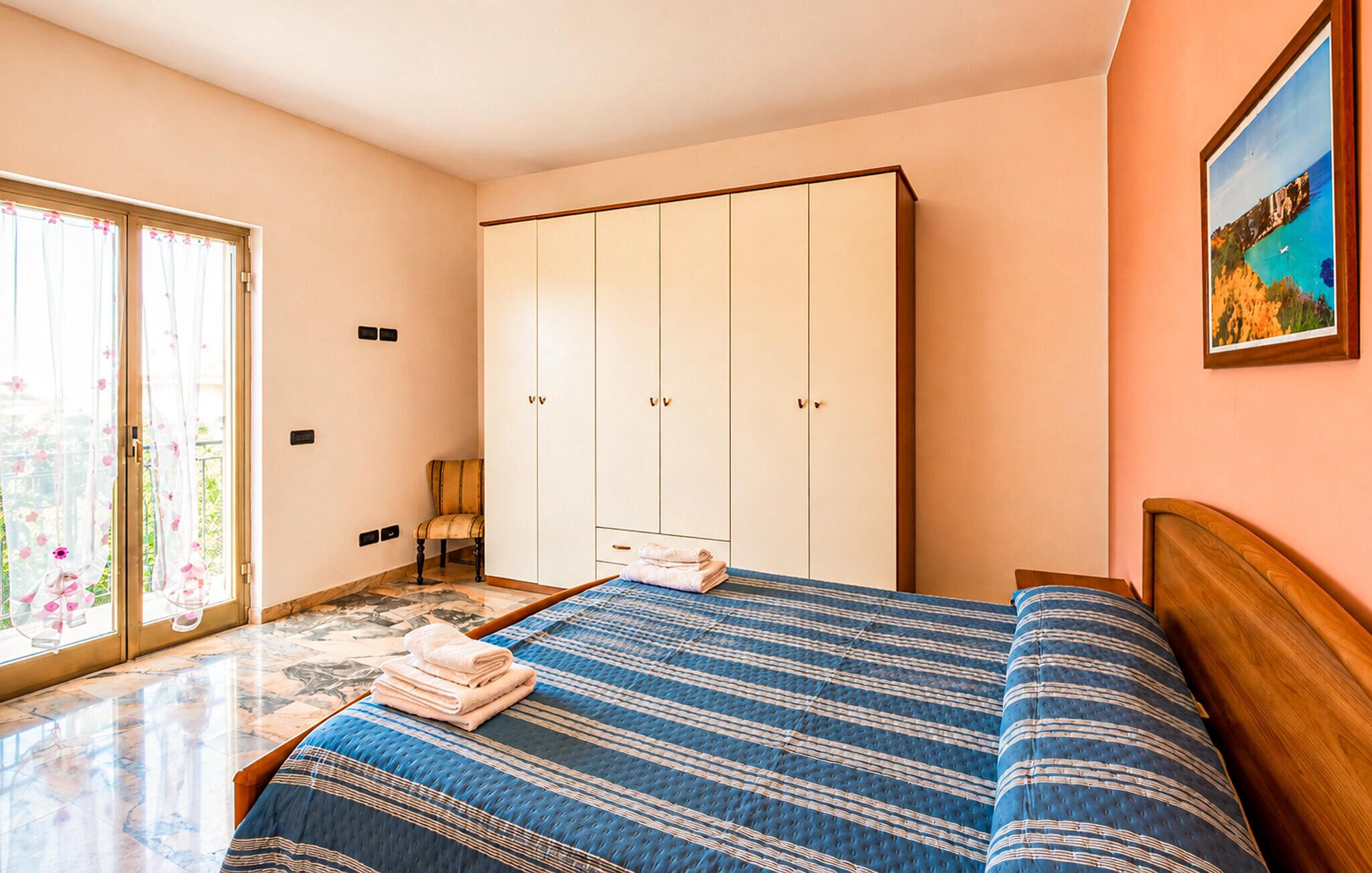 A bedroom with a bed, a wardrobe, a chair, and a painting on the wall.