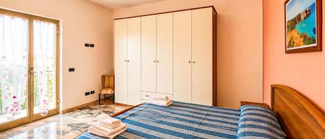 A bedroom with a bed, a wardrobe, a chair, and a painting on the wall.