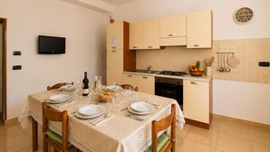 Uma sala de jantar com mesa posta para quatro, uma cozinha com fogão a gás e um relógio fixado na parede.