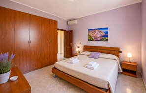 Un dormitorio con cama, armario de madera, mesitas de noche, un cuadro y una planta en maceta.