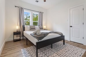 A bedroom with a bed, bedside tables, a window with curtains, a door, and a patterned rug. - Spacious 4-bedroom house in Houston Texas Hot tub/ Play room. (Houston)