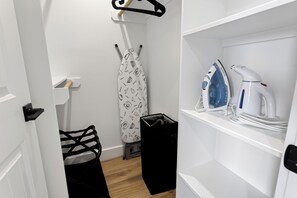 Ein Hotelzimmer mit einem weißen Kleiderschrank, einem schwarzen Kofferständer, einer schwarzen Tasche und einem Regal mit Bügeleisen und Wasserkocher.
