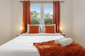 A hotel room with a large bed, two bedside lamps, and a window with curtains. - Spacious 4-bedroom house in Houston Texas Hot tub/ Play room. (Houston)