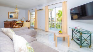 Una sala de estar moderna con sofá, mesa de comedor, televisor y balcón con cortinas.