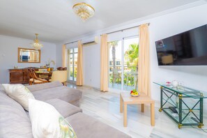 Una sala de estar moderna con sofá, mesa de comedor, televisor y balcón con cortinas.