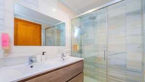Un baño moderno con lavamanos doble, un espejo grande, cerramiento de ducha de vidrio y un mueble de madera.