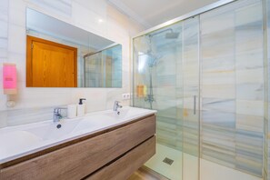 Un baño moderno con lavamanos doble, un espejo grande, cerramiento de ducha de vidrio y un mueble de madera.