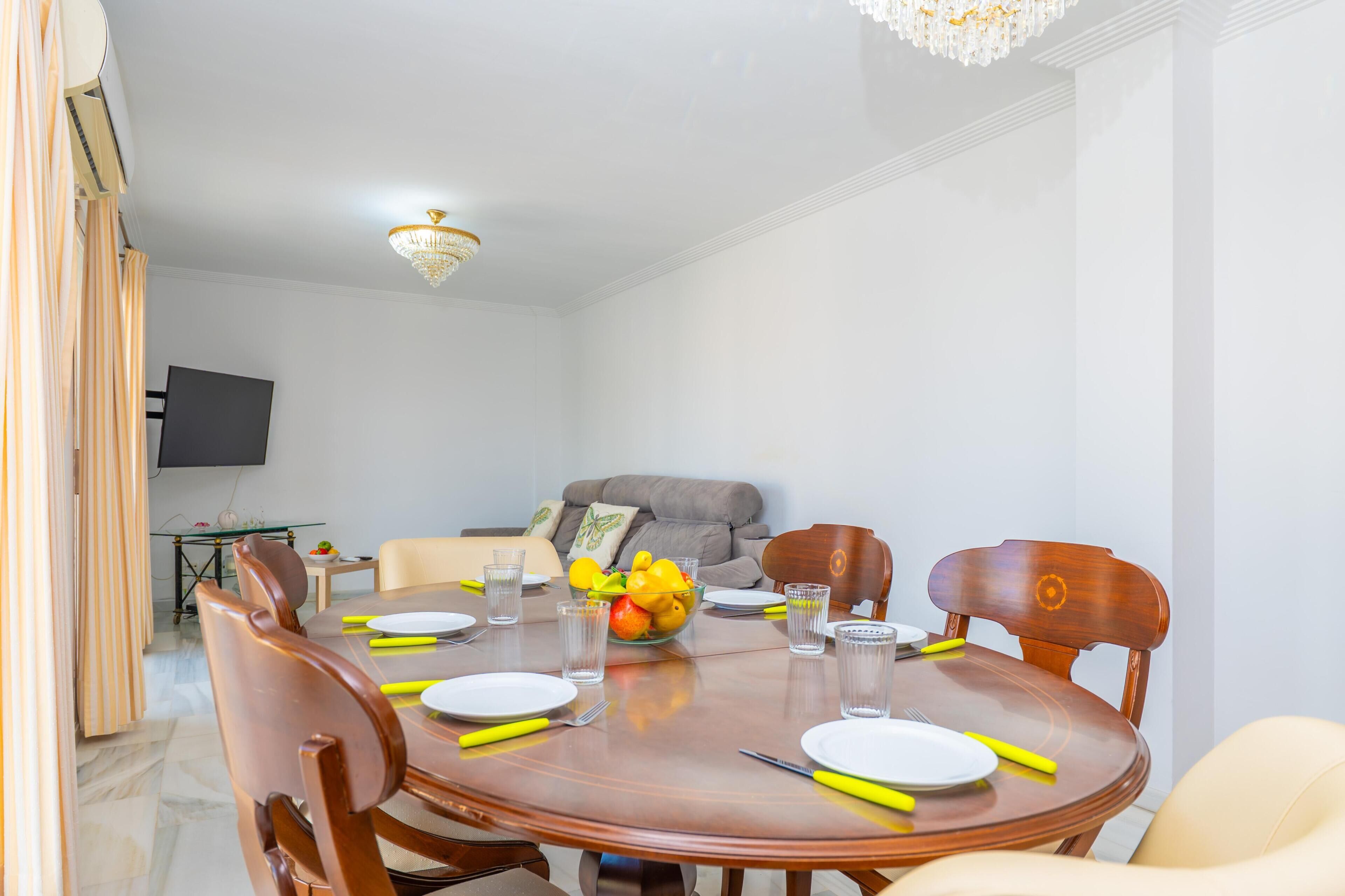 Un comedor con una mesa redonda, sillas y una araña.