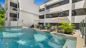 A modern building with a swimming pool, outdoor seating, and potted plants. - Palm Cove Studio with King Bed and Pool | Myrtle Studio (Palm Cove)