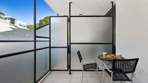 En balkon med gelænder, to stole, et lille rundt bord og et par croissanter.