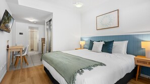 A hotel room with a bed, bedside tables, a desk with chairs, and a door leading to a bathroom. - Palm Cove Studio with King Bed and Pool | Oliva Tides Studio (Palm Cove)