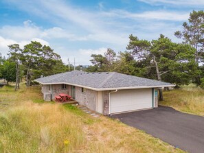 A single-story building with a garage, a red bench, and a grassy area. - Kiwanda Cottage - Steps to the beach - Dogs OK (Pacific City)