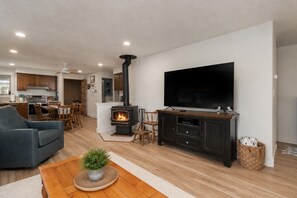 A modern living room with a fireplace, a flat-screen TV, and a dining area with wooden furniture. - Kiwanda Cottage - Steps to the beach - Dogs OK (Pacific City)