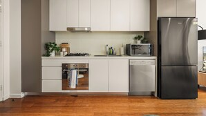 Una cuina moderna amb armaris blancs, electrodomèstics d'acer inoxidable i un rentaplats integrat.