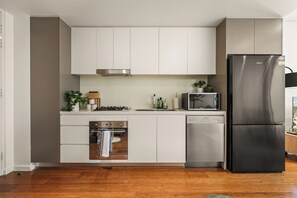 Una cuina moderna amb armaris blancs, electrodomèstics d'acer inoxidable i un rentaplats integrat.