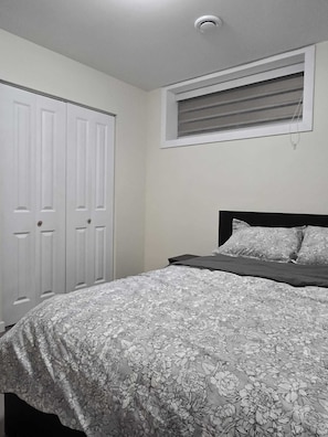 Ein Schlafzimmer mit einem Bett, einem Fenster mit Jalousien und einer weißen Tür.