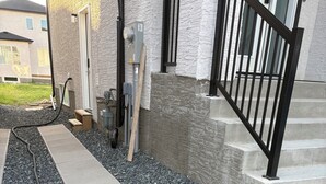 Un chemin menant à l’entrée d’un bâtiment, avec des marches et une rambarde en métal.