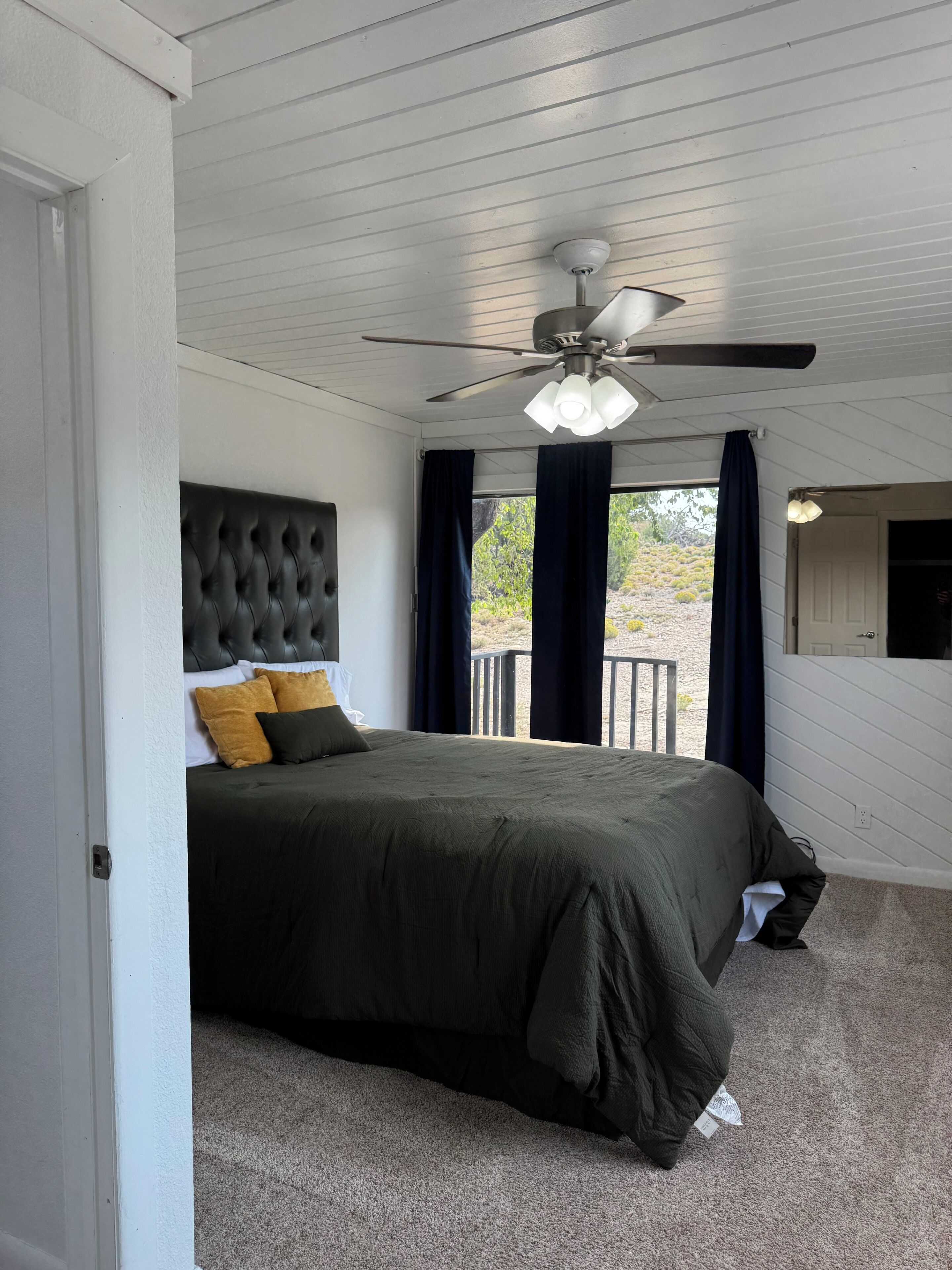 A bedroom with a bed, a ceiling fan, and a view through the window.