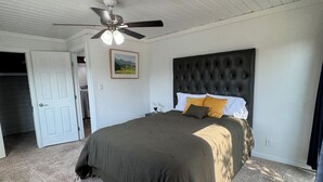A bedroom with a large bed, a ceiling fan, and a door leading to another room.