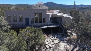 A modern building with a flat roof, large windows, and a balcony overlooking a rocky terrain with sparse vegetation.