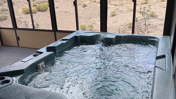A hot tub with a view of a desert landscape through large windows.