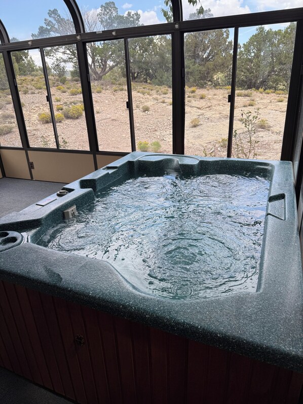 A hot tub with a view of a desert landscape through large windows.