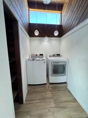 A laundry room with two washing machines and a dryer, wooden ceiling, and a skylight.