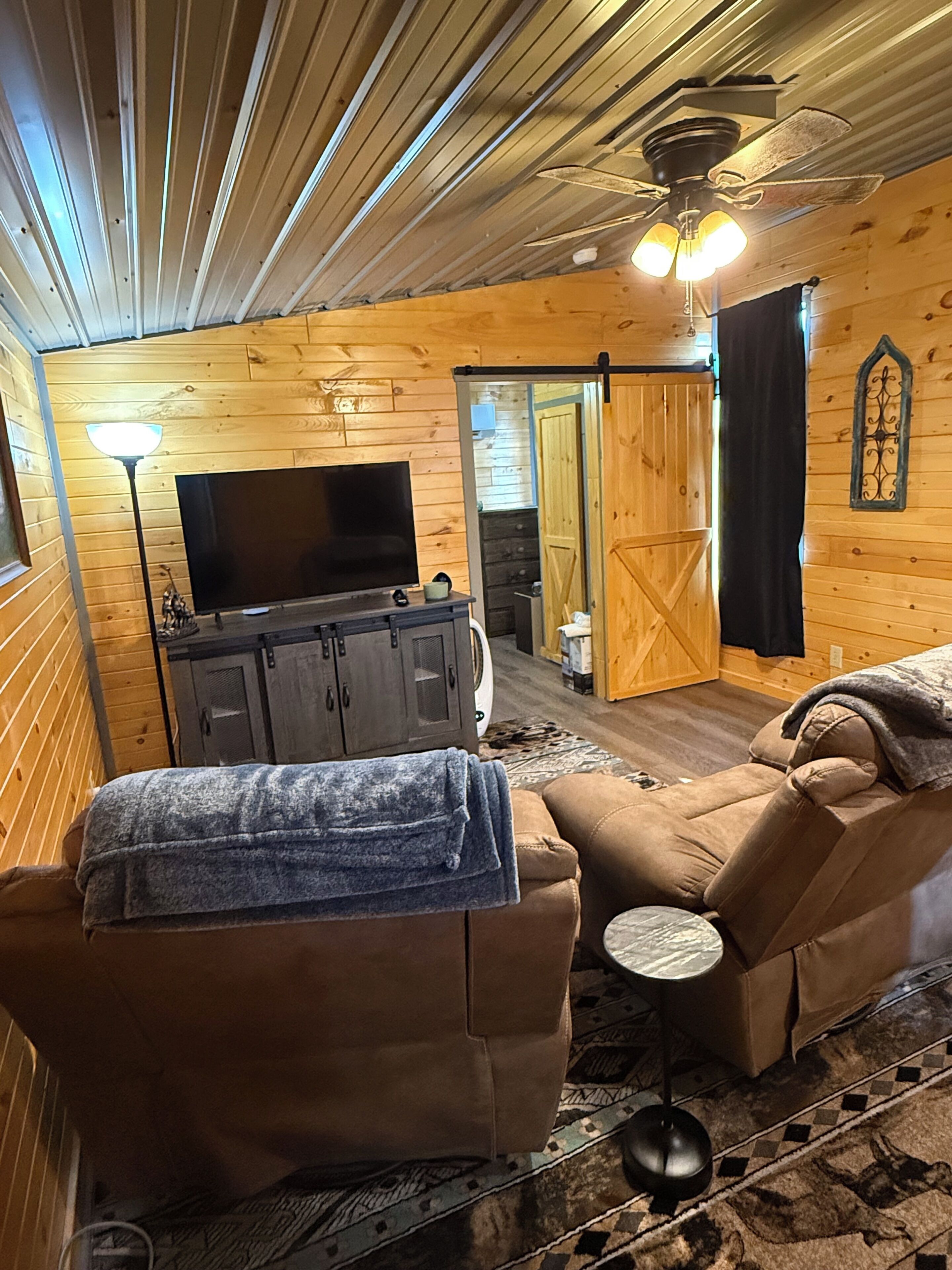 A cozy cabin interior with a sofa, a television, a cabinet, and a ceiling fan.