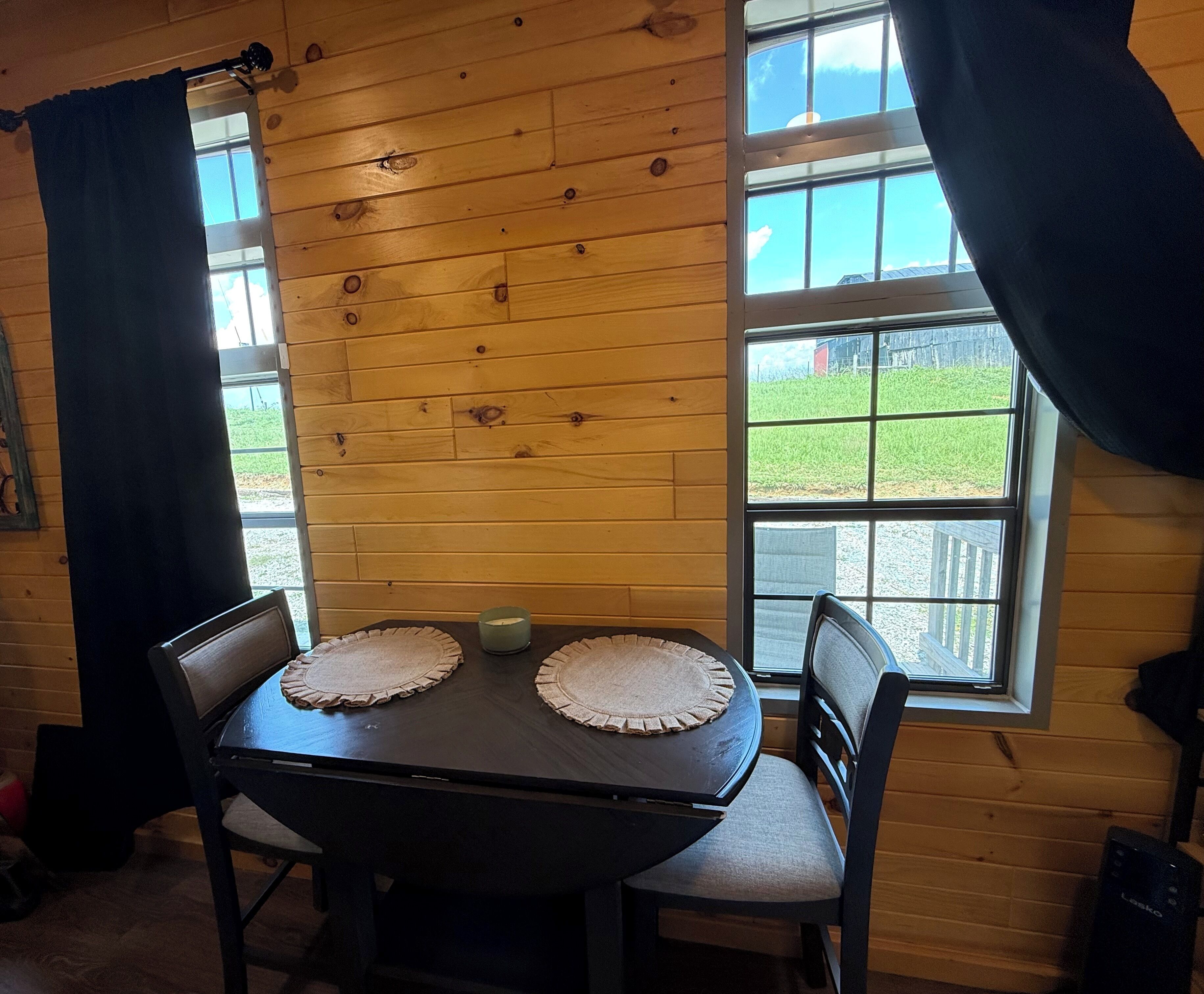Een kamer met houten lambrisering, een tafel en stoelen, een raam met gordijnen en uitzicht op een gazon.