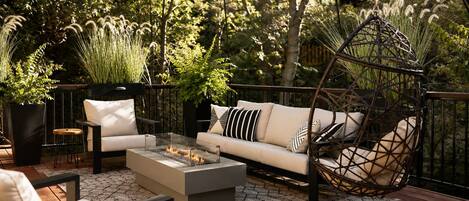 An outdoor seating area with a sofa, chairs, a fire pit, and a hanging swing.