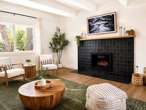 A living room with a fireplace, a large window, and a view of the outdoors. - EV charger, hot tub and A/C Cozy 3-bedroom cabin in charming Lake Arrowhead (Lake Arrowhead)