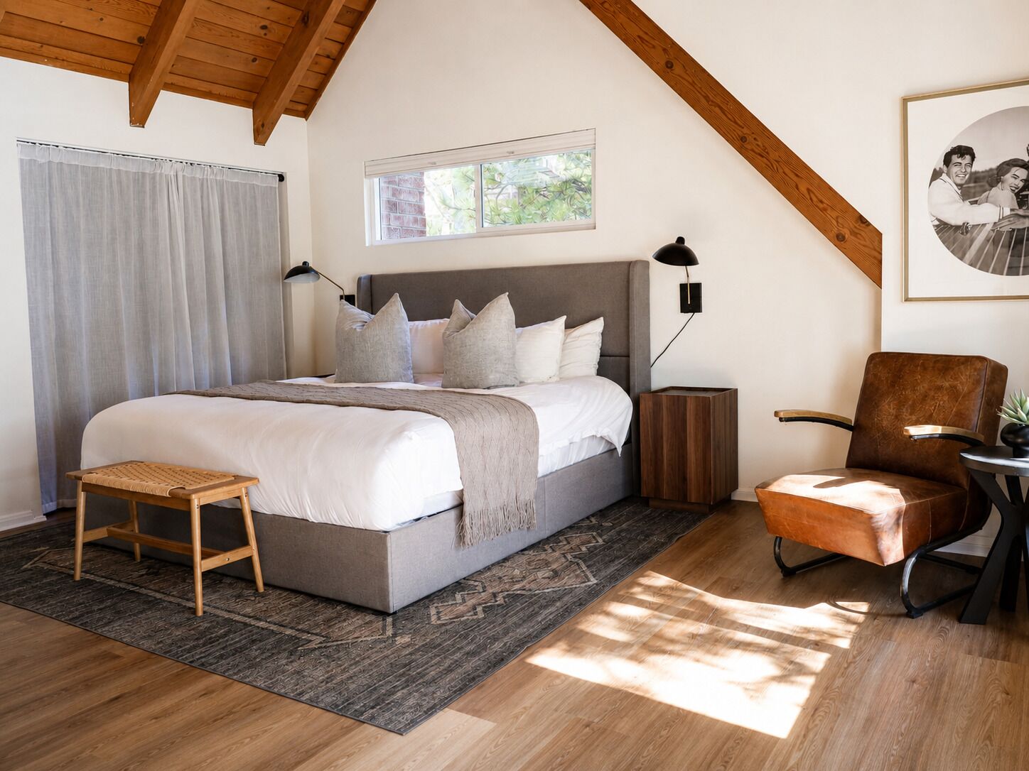 A bedroom with a large bed, a wooden bench, a chair, a nightstand, and a window.