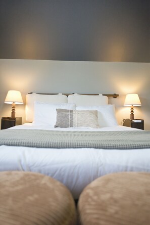 A neatly made bed with white linens and a grey throw blanket, flanked by two bedside lamps on matching nightstands. - Mins to RRG | Hot Tub, Game Room, Fire Pit (Stanton)