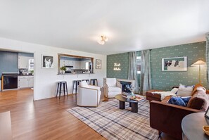 A modern living room with a sofa, armchairs, a coffee table, and a dining area with a kitchen in the background. - Mins to RRG | Hot Tub, Game Room, Fire Pit (Stanton)