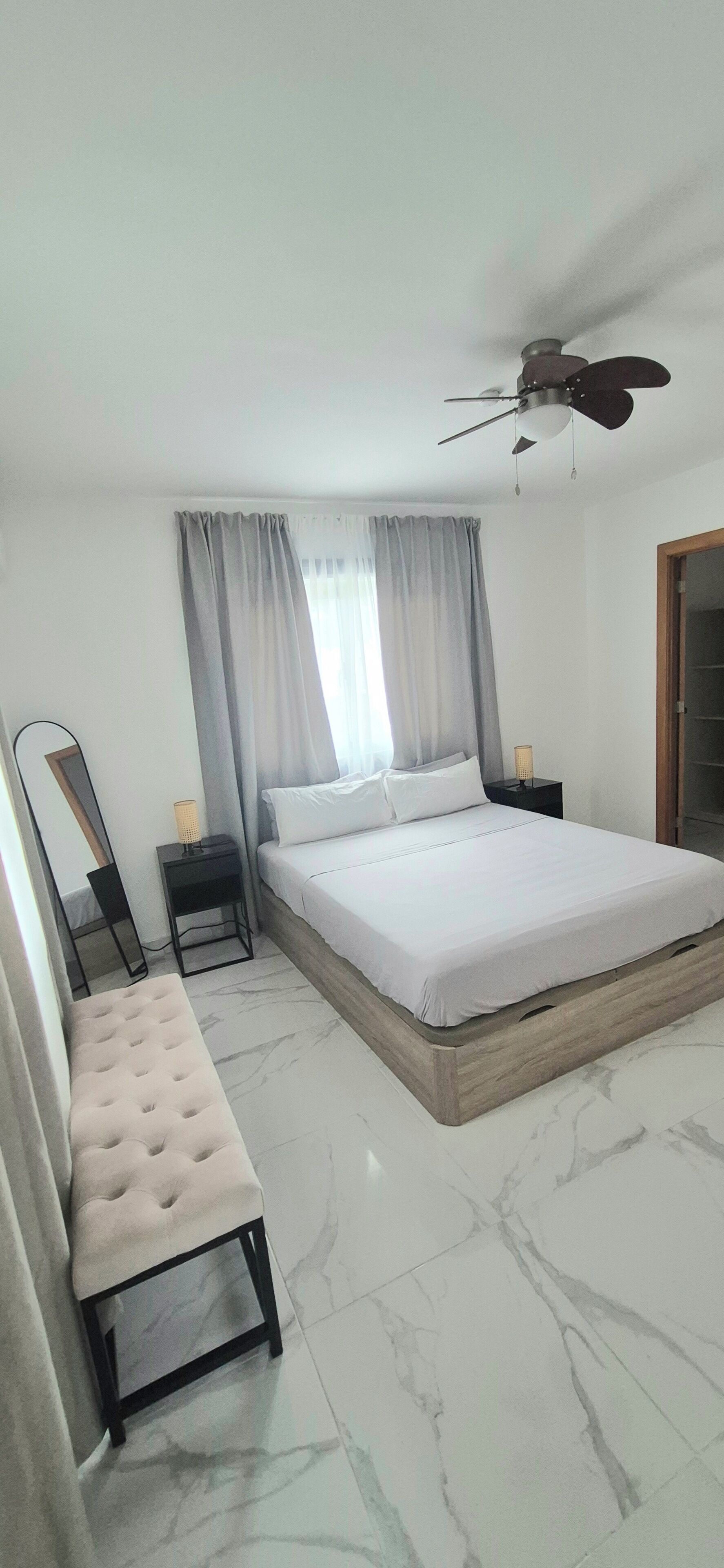 A bedroom with a bed, a bench, a nightstand, a mirror, and a ceiling fan.